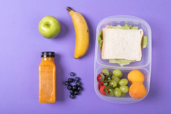 俯瞰水果和果汁瓶子三明治在紫色背景的松饼盒里 健康食品 水果和包装好的午餐 — 图库照片