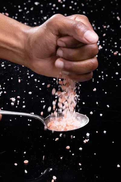黒人を背景にスプーンでヒマラヤ塩を振りかけるアフリカ系アメリカ人男性の作物の手 素材や食品岩塩調味料の概念を変えずに — ストック写真