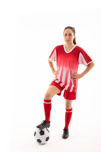 腰に手を置きサッカーボールに足で立っている白人の若い女性選手の肖像画 白い背景変更なしスポーツユニフォームコピースペースアスリート女子サッカー — ストック写真