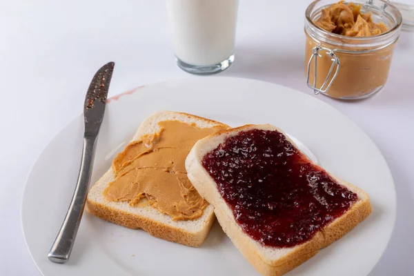 テーブルの上にミルクグラスと瓶でプレートにオープンフェイスピーナッツバターとゼリーサンドイッチのクローズアップ 変更なしピーナッツバターとゼリーサンドイッチ健康食品保存準備朝食 — ストック写真