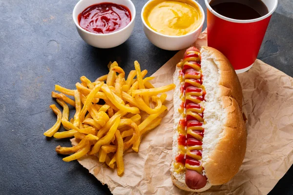 High angle view of hot dog with french fries, sauces and drink on table. unaltered, unhealthy food, meat, bread, sausage and fast food.
