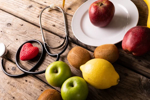 Hochwinkelaufnahme Verschiedener Früchte Mit Stethoskop Und Herzform Auf Holztisch Unverändertes — Stockfoto