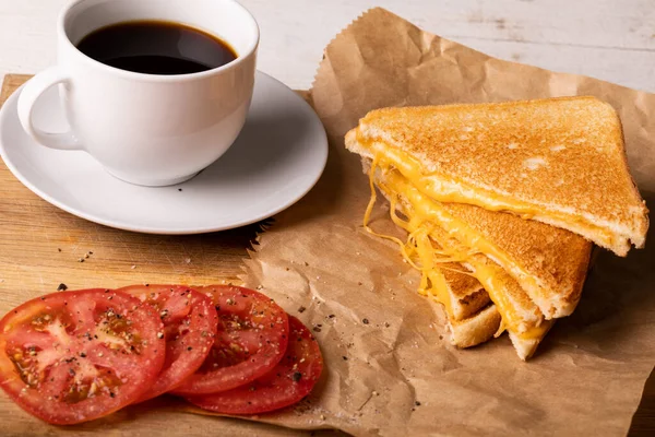 ワックスペーパー上のチーズサンドイッチでトマトスライスとフレッシュブラックコーヒーの高い角度ビュー 変化のない食べ物不健康な食事や軽食の概念 — ストック写真