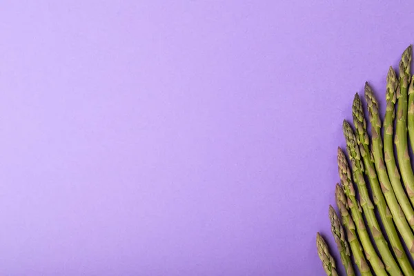 紫色の背景に並んで配置された生のアスパラガスとコピースペースの直接上のビュー 変化のない食品健康的な食生活有機的な概念 — ストック写真