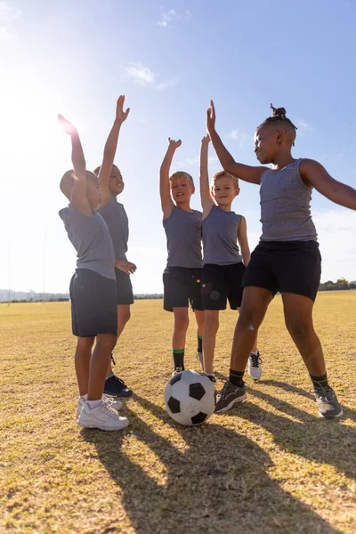 サッカーに立ち上がる腕を持つ多人種の小学生が空に対して提出しました 子供時代教育スポーツトレーニングバックライトチームスポーツスポーツ活動のコンセプト — ストック写真