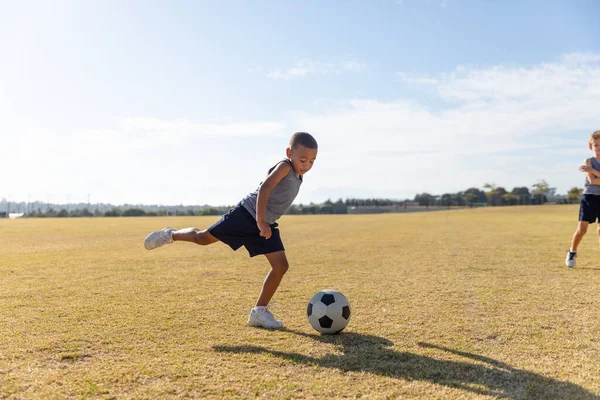Biracial Základní Školák Kopání Fotbalový Míč Při Hraní Hřišti Proti — Stock fotografie