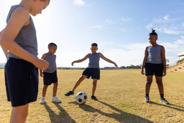 Wielorasowych Uczniów Elementarnych Patrząc Birasowy Chłopiec Kopanie Piłki Nożnej Boisku — Zdjęcie stockowe
