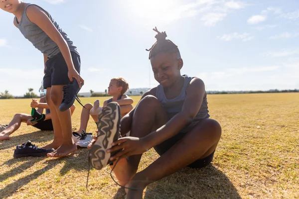 Estudiantes Primaria Multirraciales Quitándose Zapato Mientras Están Sentados Campo Contra — Foto de Stock