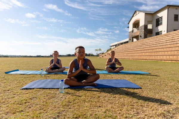 多种族小学生坐在操场上的垫子上沉思 运动训练 瑜伽和体育概念 — 图库照片