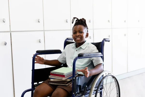 車椅子に座って本を持つアフリカ系アメリカ人の小学生の笑顔の肖像画 子供時代障害身体障害教育学校の概念に立ち返り — ストック写真