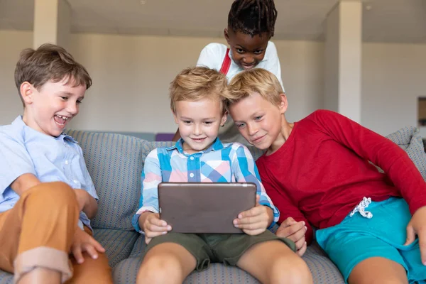 学校のソファに座っている間 多人種の小学生がデジタルタブレットを見て笑っています 変化のない子供時代を共に無線技術教育を学校のコンセプトに戻し — ストック写真