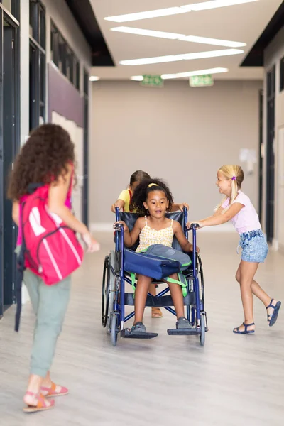 Multiracial Elementary Schoolgirls Holding Female Classmate Wheelchair Corridor Unaltered Childhood — Stock Photo, Image