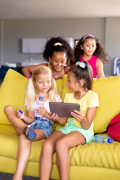 白种人小学生坐在沙发上向多种族同学展示数码平板电脑 无线技术 教育和重返校园的概念 — 图库照片