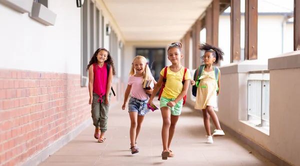 Full Length Happy Multiracial Elementary Schoolgirls Walking Corridor Unaltered Childhood — Stock Photo, Image