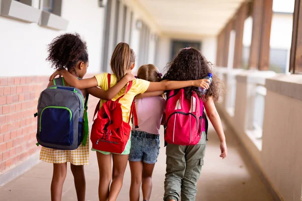 Rear View Multiracial Elementary Schoolgirls Backpacks Arm Walking Corridor Unaltered — Stock Photo, Image