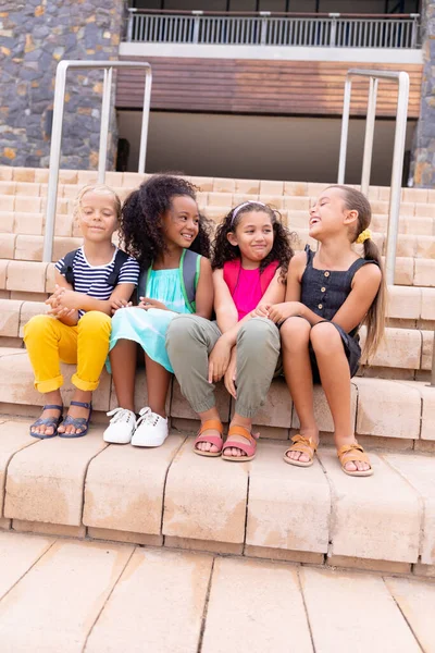 Повна Тривалість Багаторасових Усміхнених Початкових Школярок Сидять Сходах Проти Шкільного — стокове фото