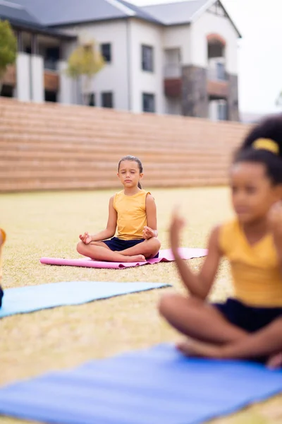 Escolas Primárias Multirraciais Meditando Enquanto Sentado Tapete Ioga Contra Escola — Fotografia de Stock