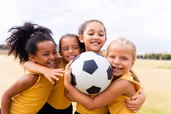 Gelukkige Multiraciale Basisschoolmeisjes Met Voetbal Omarmen Terwijl Grond Staan Ongewijzigd — Stockfoto