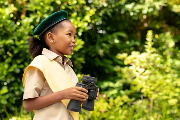在森林里微笑着身穿制服的美国女童子军拿着双筒望远镜 童年时代 冒险和侦察 — 图库照片