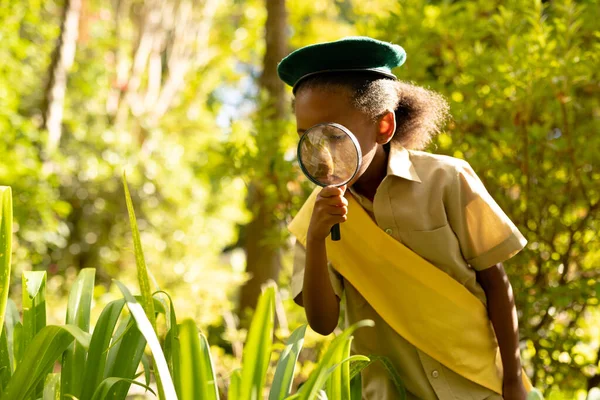 森の虫眼鏡を通して植物を見て制服を着たアフリカ系アメリカ人のスカウトの女の子 変更されていない少女のスカウト 子供時代 スカウト — ストック写真