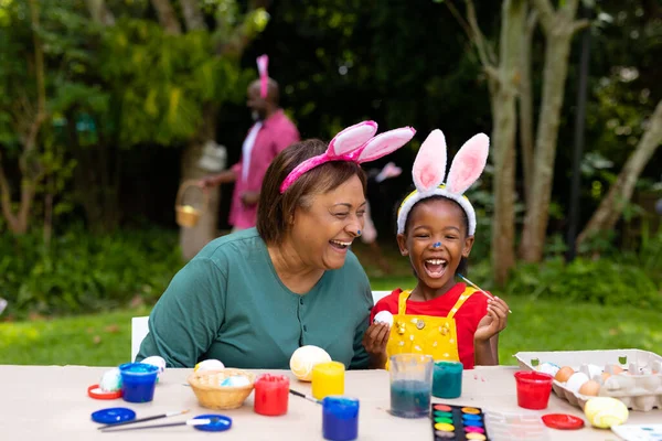 喜庆的非洲裔美国女孩和祖母在复活节涂蛋时戴着小兔子耳朵 生活方式 复活节 文化和假日观念不变 — 图库照片