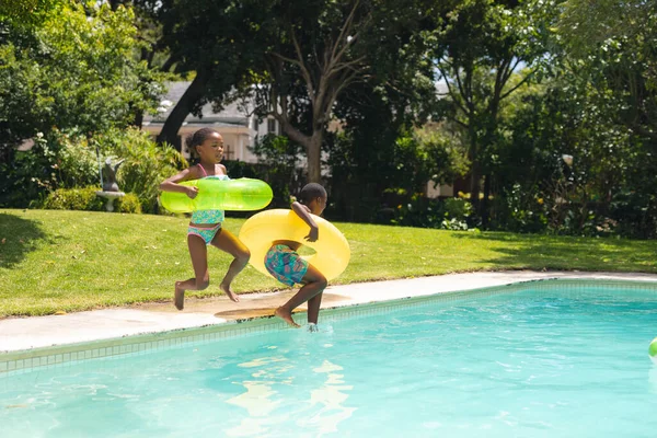 アフリカ系アメリカ人の兄弟は晴れた日にプールでインフレータブルリングでジャンプします 変わらないライフスタイル家族子供時代楽しいレジャー週末のコンセプト — ストック写真