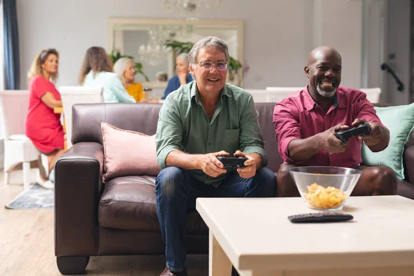 Multiraciale Oudere Mannelijke Vrienden Spelen Videospel Terwijl Vrouwen Achtergrond Thuis — Stockfoto