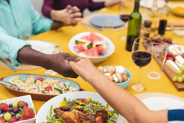 多种族的高级男女朋友牵着手 在餐桌前祈祷 不变的 不变的生活方式 退休和后院派对 — 图库照片