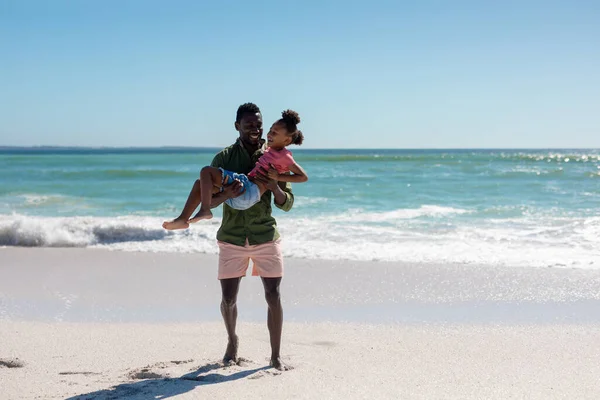 Pełna Długość Szczęśliwego Afrykańskiego Mężczyzny Niosącego Córkę Plaży Przeciwko Niebu — Zdjęcie stockowe