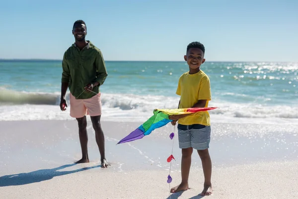 ビーチで父親の近くに立っている間にカイトを保持アフリカ系アメリカ人の少年笑顔の肖像画 変わることのない家族生活一緒に楽しむ休日の概念 — ストック写真
