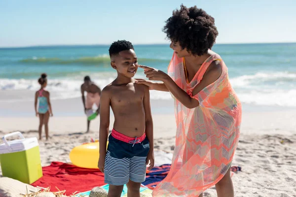 アフリカ系アメリカ人女性は息子の顔に化粧水を塗り 父親と娘はビーチで遊ぶ 変わることのない家族生活一緒に楽しむ休日の概念 — ストック写真