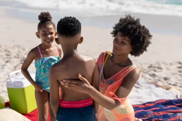 Uśmiechnięta Afroamerykanka Pocierająca Plecami Syna Bez Koszulki Plaży Bez Zmian — Zdjęcie stockowe