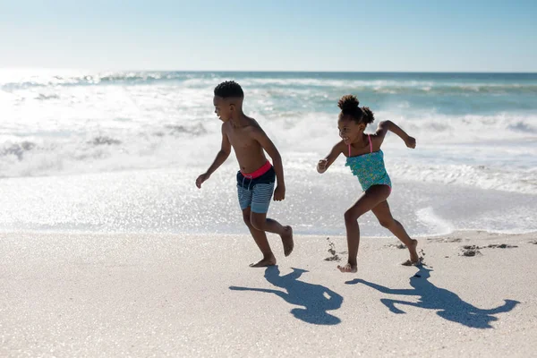 晴れた日にビーチで海岸を走っているアフリカ系アメリカ人の男の子と女の子の完全な長さ 変わることのない家族子供時代一緒に楽しむ休日のコンセプト — ストック写真