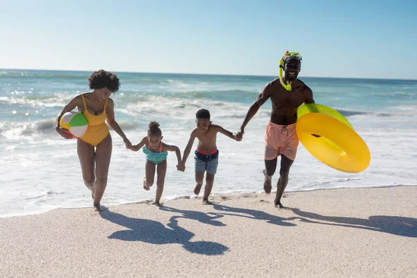 澄んだ空を背景にビーチで一緒に走りながら 幸せなアフリカ系アメリカ人家族が手をつないでいます 変わることのない家族生活一緒に楽しむ休日の概念 — ストック写真