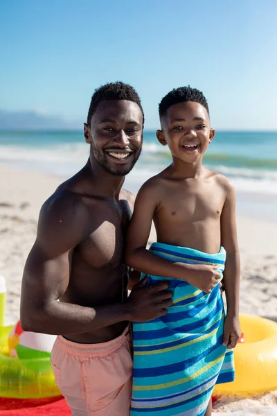 在阳光灿烂的日子里 非洲裔美国人赤身裸体的父亲和儿子在沙滩上与蓝天相映成趣的画像 不变的家庭 生活方式 享乐及假日概念 — 图库照片