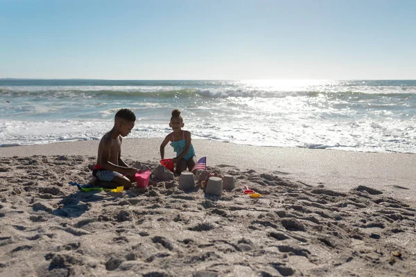 晴れた日には アフリカ系アメリカ人の男の子と女の子がビーチで一緒に砂の城を作っています 変わることのない家族子供時代一緒に楽しむ休日のコンセプト — ストック写真