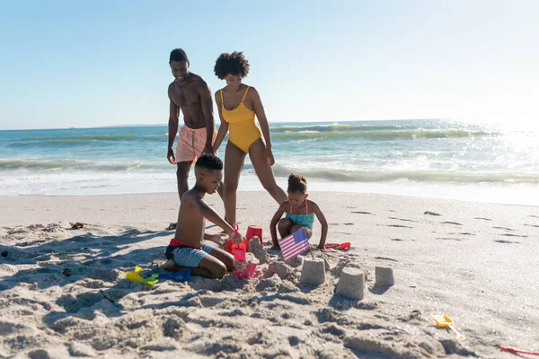 ビーチで一緒に砂の城を作る子供たちによって歩く幸せなアフリカ系アメリカ人の両親 変わることのない家族生活一緒に楽しむ休日の概念 — ストック写真