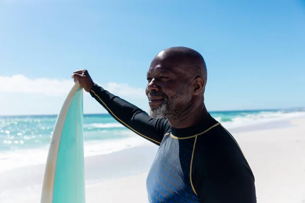 晴れた日にビーチを眺めながらサーフボードを持っているアフリカ系アメリカ人のはげ先輩を笑っています 変化のないアクティブなライフスタイル水生スポーツ休日の概念 — ストック写真