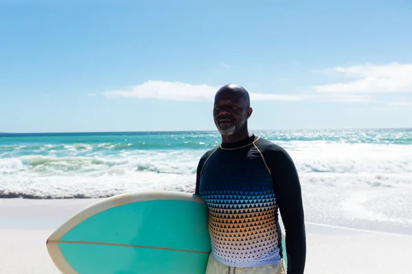 アフリカ系アメリカ人の老人は晴れた日にビーチでサーフボードを持って空に向かって引退した 変化のないアクティブなライフスタイル水生スポーツ休日の概念 — ストック写真