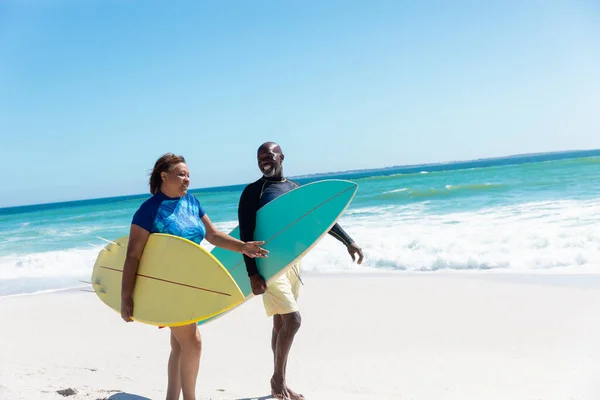 アフリカ系アメリカ人のシニアカップルは コピースペースのある青い空に対してビーチでサーフボードを歩いています 変更されず団結し積極的なライフスタイル水生スポーツ休日の概念 — ストック写真