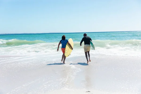 アフリカ系アメリカ人のシニアカップルは コピースペースのあるビーチで波に向かって走るサーフボードを持っている 変更されず団結し積極的なライフスタイル水生スポーツ休日の概念 — ストック写真
