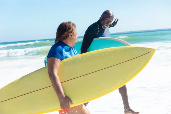 アフリカ系アメリカ人は 晴れた日にビーチでサーフボードを持っている間に話して引退した 変更されず団結し積極的なライフスタイル水生スポーツ休日の概念 — ストック写真