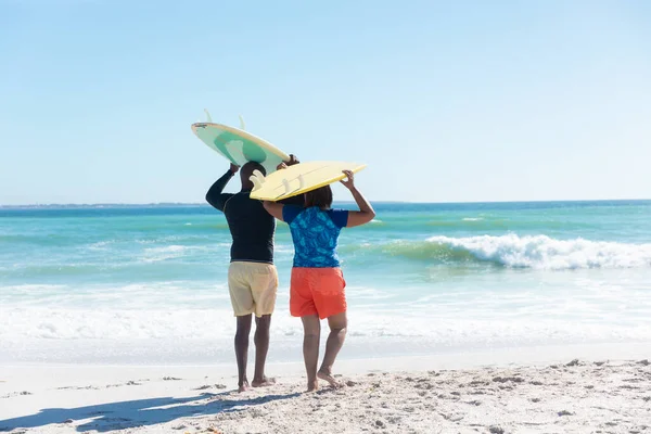 アフリカ系アメリカ人のシニアカップルは コピースペースを持つ空に対してビーチでサーフボードを運んでいます 変更されず団結し積極的なライフスタイル水生スポーツ休日の概念 — ストック写真
