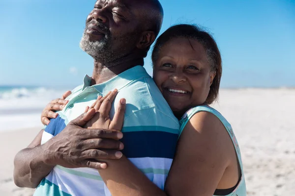 阳光灿烂的日子里 在海滩上微笑着从后面拥抱男人的退休老年非洲女人 不变的 聚会的 生活方式的 享受的和假日的概念 — 图库照片