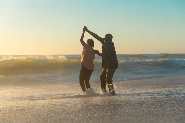 幸せなアフリカ系アメリカ人の引退した老夫婦は日没の間に空に対してビーチで海岸で踊る 変わらない愛 ライフスタイル 楽しみと休日のコンセプト — ストック写真