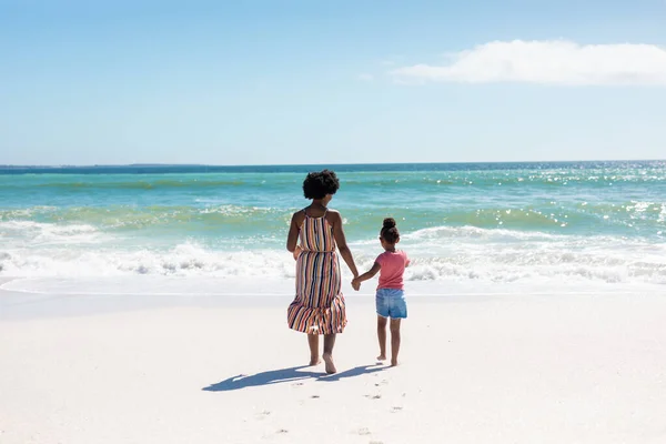 ビーチで海に向かって歩いている間に手を取り合っているアフリカ系アメリカ人の母親と娘の背面図 変わることのない家族生活一緒に楽しむ休日の概念 — ストック写真