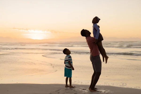 アフリカ系アメリカ人の息子は 日没時に海に立っている間に父親が女の子を拾うのを見た 変わらないビーチ 子供時代 ライフスタイル 楽しみそして休日 — ストック写真