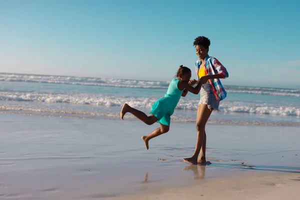幸せなアフリカ系アメリカ人の若い女性が海と澄んだ空に対して海岸で遊び心のある娘を回転させます コピースペース 変更なし ビーチ 子供時代 一緒に 楽しみ ライフスタイル — ストック写真
