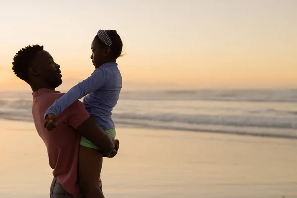 Joven Afroamericano Recogiendo Hija Mientras Está Pie Contra Mar Cielo — Foto de Stock