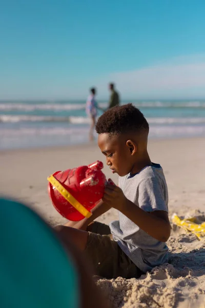 海と青い空に対してビーチで砂で遊んでいるアフリカ系アメリカ人の少年の側面図 コピースペース 子供時代 変わらない ビーチ ライフスタイル 楽しみと休日の概念 — ストック写真